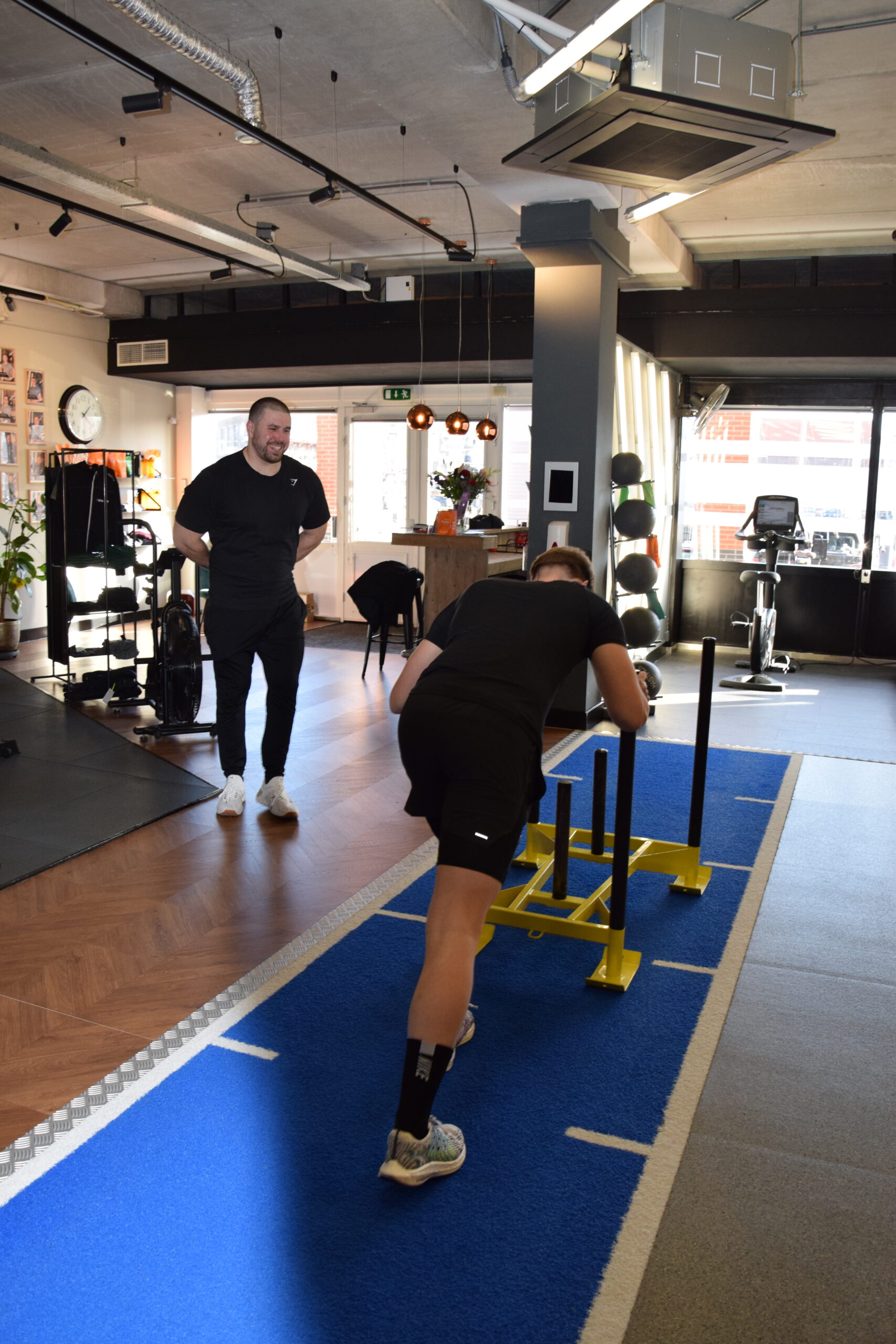 Personal trainer/coach coaching a client that is doing a sled push during a hiit work out.