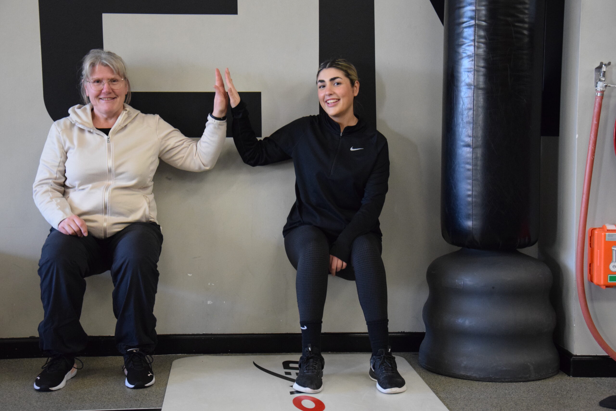 2 clients having fun and high fiving whilst performing a wall sit during a duo HIIT PT session